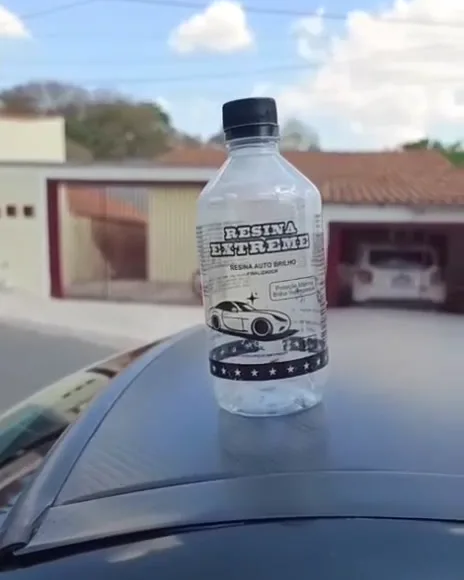 Frasco da Resina Extreme sobre o capô preto de um carro, com o céu refletido na pintura